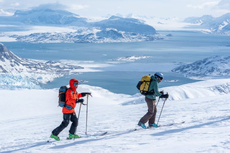 Skier on a rugged Arctic mountain peak preparing for a steep off-piste run directly to the sea. Exclusive ski and sail expedition in Svalbard far from the crowds
