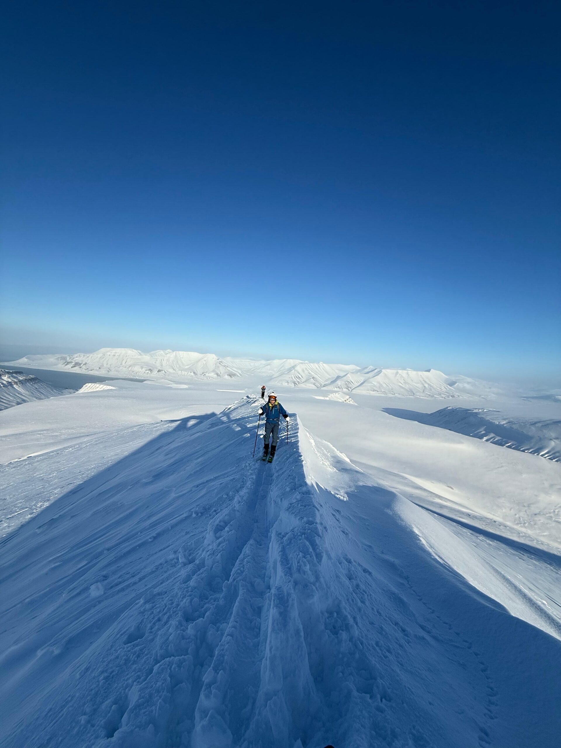 Ski touring with climbing skins on snowy Arctic mountains in Svalbard during sunny winter ski season