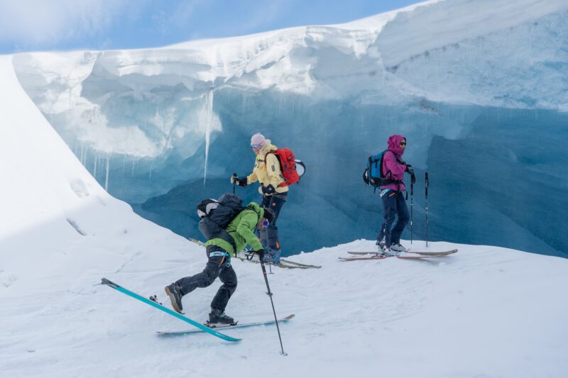 Ski tourers exploring a glowing blue ice cave on a glacier during a ski and sail expedition in Svalbard
