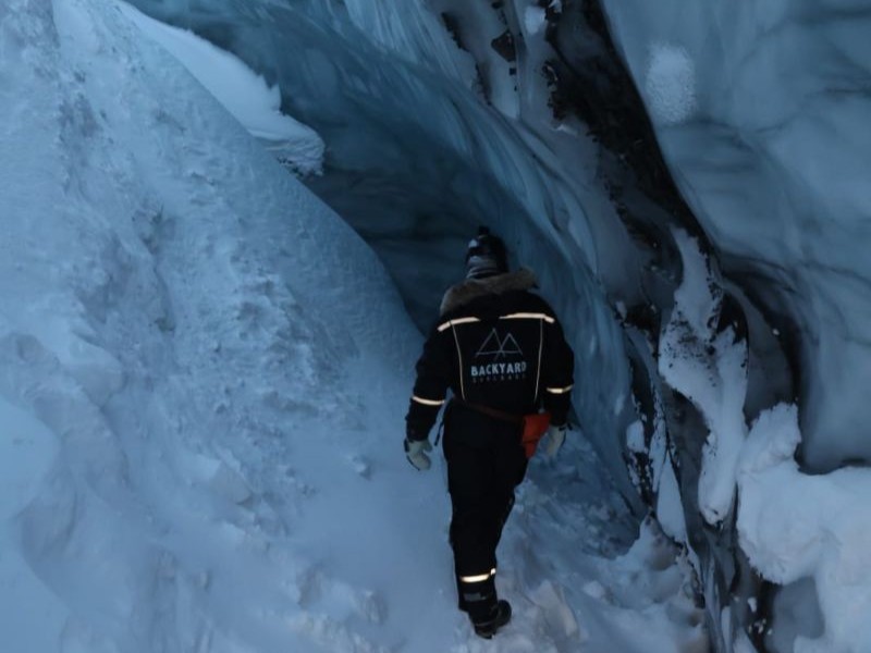 Atour guide in full Arctic gear leading a small group on snowmobile safari tow a hidden ice cave