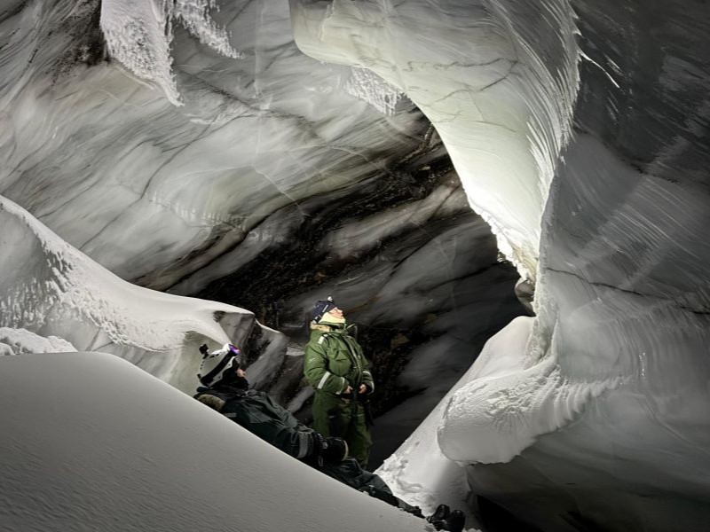 Snowmobiles parked outside the entrance while small group explore the inside of an ice cave in Svalbard