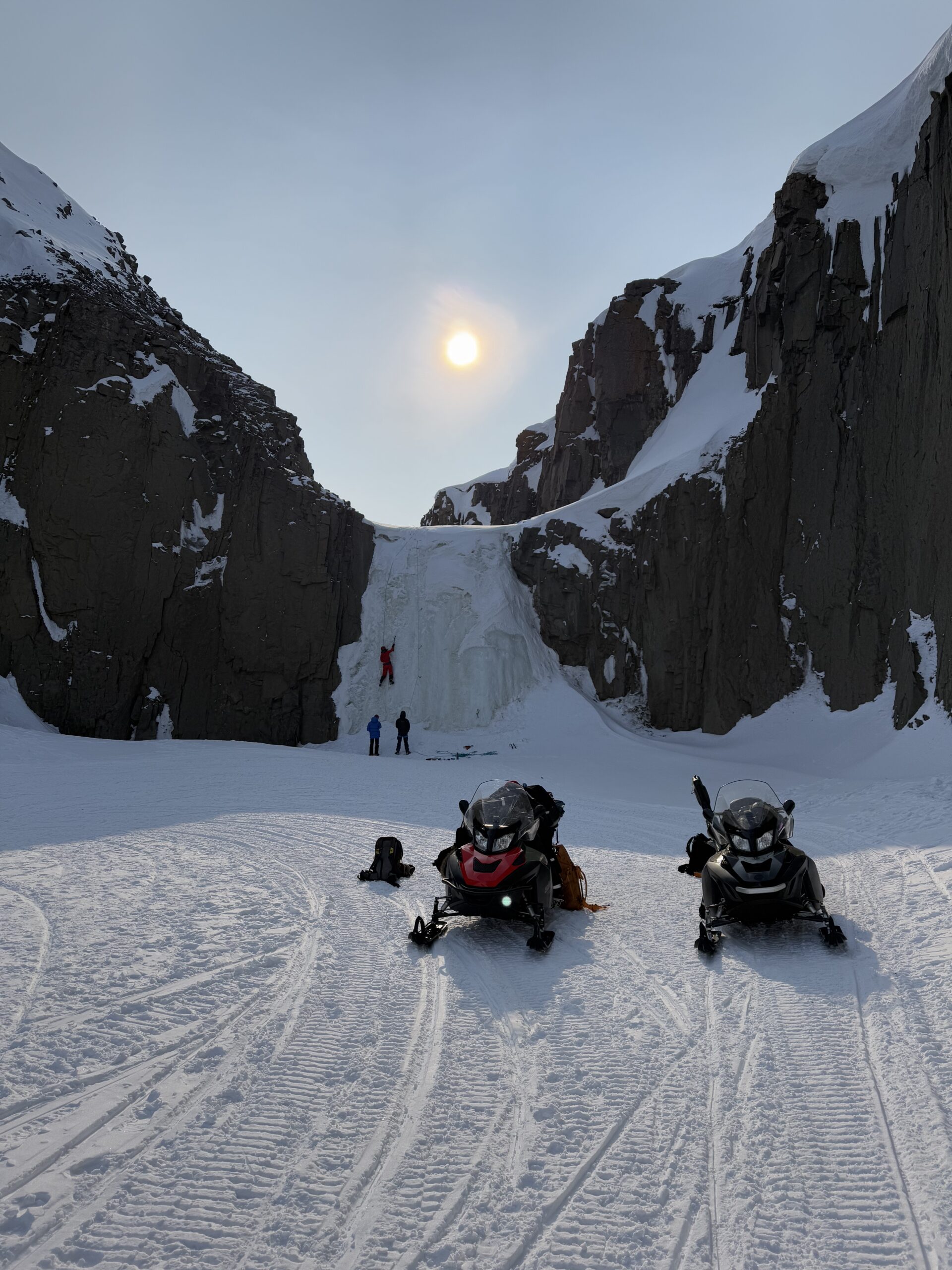 Snowmobiles parked in the Arctic landscape to a frozen waterfall for an ice climbing adventure on Svalbard