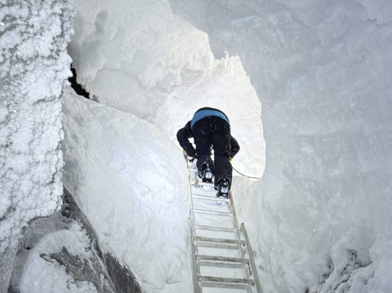 An explorer climbing down the ladder into a magical glacier ice cave on the Backyard Svalbard tour