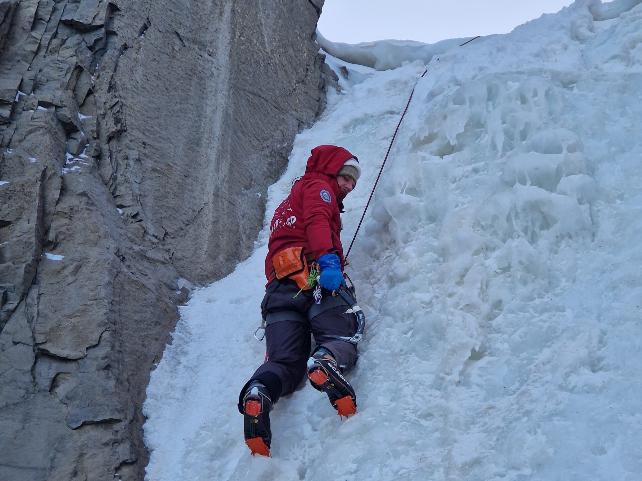 Ice climber using crampons and ice axe climbing a frozen waterfall on Svalbard