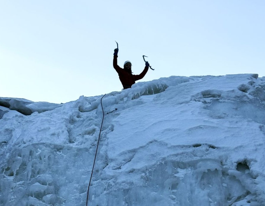 Ice climber standing on top of a massive frozen waterfall during Svalbard winter