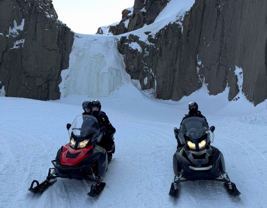 Snowmobiles parked in front of frozen waterfall. Join a full day adventure on Svalbard with ice climbing adventure