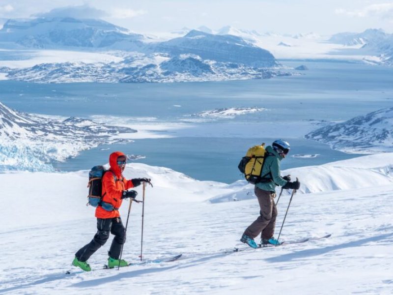 Skier on a rugged Arctic mountain peak preparing for a steep off-piste run directly to the sea. Exclusive ski and sail expedition in Svalbard far from the crowds